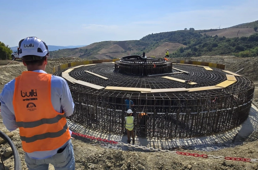 lavoratore di spalle davanti cantiere base pala eolica